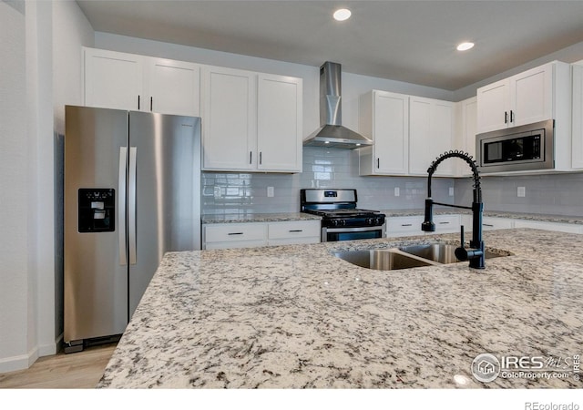 kitchen featuring wall chimney exhaust hood, sink, white cabinetry, light stone counters, and appliances with stainless steel finishes