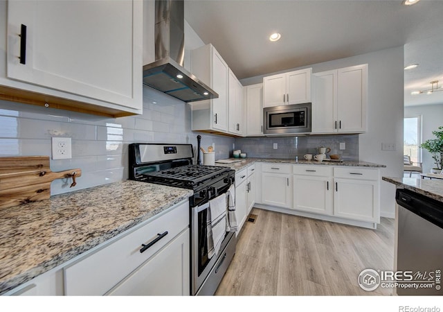 kitchen featuring white cabinets, stainless steel appliances, decorative backsplash, and wall chimney range hood