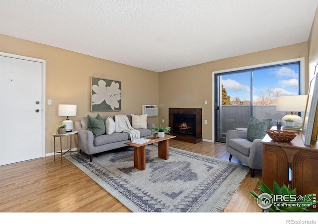 living room with a wall unit AC, a textured ceiling, and light wood-type flooring