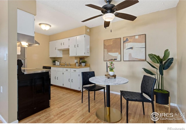 kitchen featuring range hood, white cabinetry, sink, light hardwood / wood-style floors, and a textured ceiling