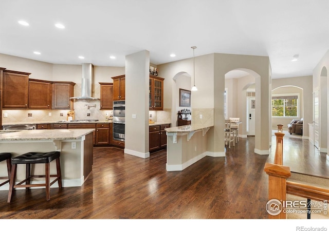 kitchen with light stone countertops, stainless steel appliances, a breakfast bar, and wall chimney exhaust hood