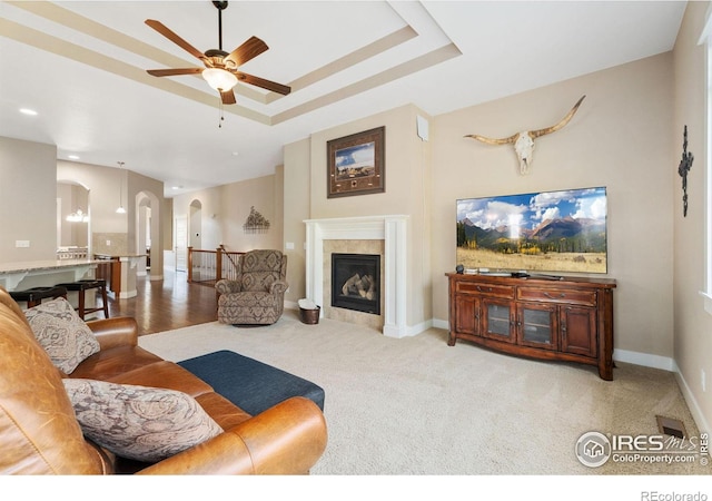 living room featuring a raised ceiling, ceiling fan, light carpet, and a fireplace