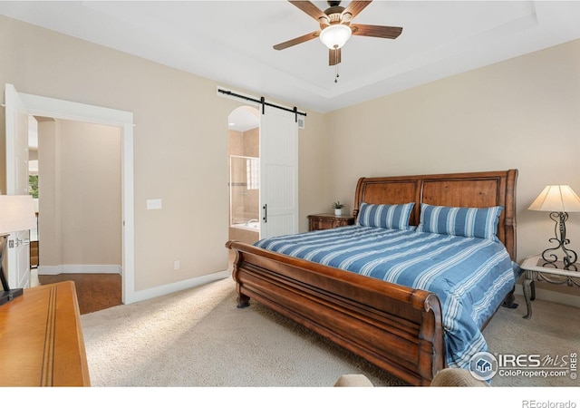 bedroom with ceiling fan, ensuite bathroom, a barn door, and carpet flooring