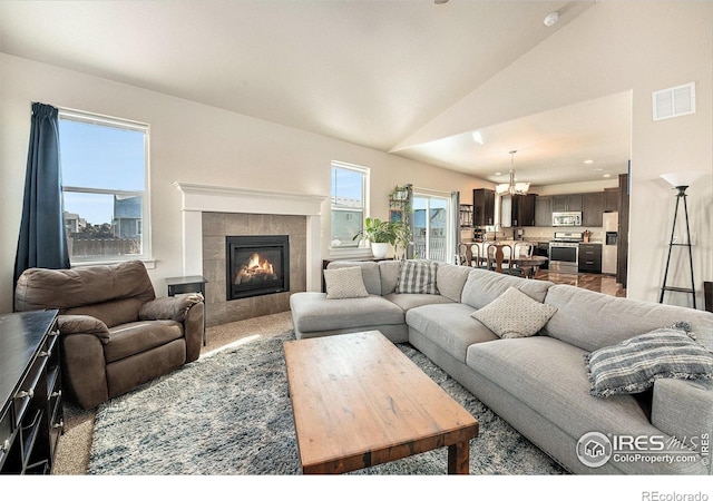 living room with lofted ceiling, a tiled fireplace, and plenty of natural light