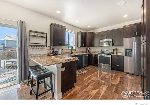 kitchen featuring dark brown cabinetry, stainless steel appliances, dark hardwood / wood-style floors, and kitchen peninsula