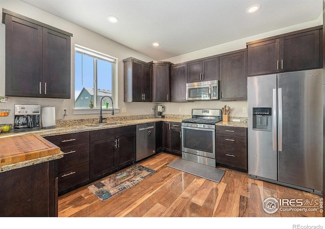 kitchen featuring appliances with stainless steel finishes, sink, dark brown cabinets, and light wood-type flooring