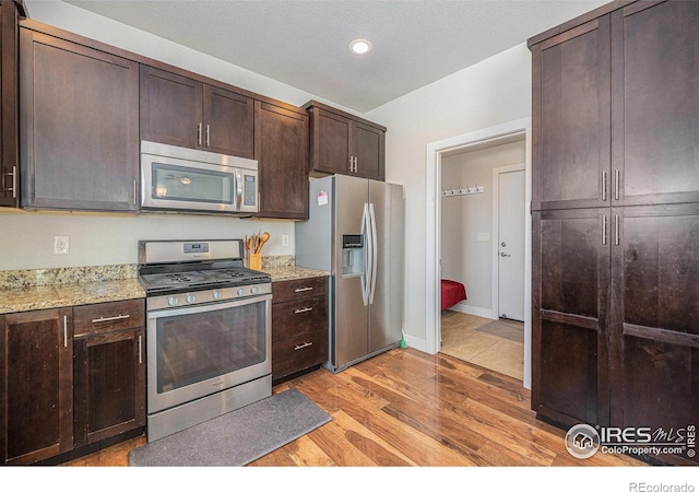 kitchen featuring dark brown cabinets, light wood-type flooring, light stone countertops, and appliances with stainless steel finishes