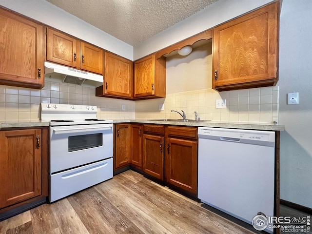 kitchen featuring sink, white appliances, tasteful backsplash, light hardwood / wood-style floors, and a textured ceiling