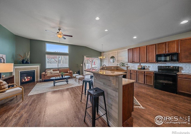 kitchen featuring vaulted ceiling, decorative light fixtures, a breakfast bar area, a kitchen island with sink, and black appliances