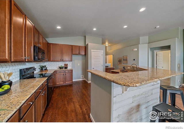 kitchen featuring tasteful backsplash, light stone countertops, a breakfast bar area, and black appliances