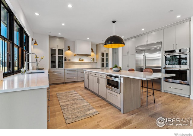 kitchen with sink, built in appliances, light hardwood / wood-style flooring, pendant lighting, and a large island