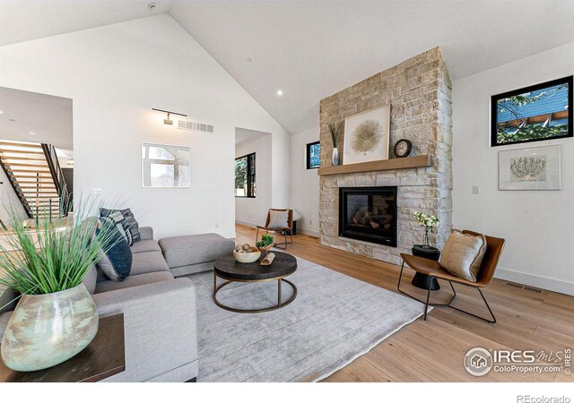 living room featuring a stone fireplace, high vaulted ceiling, and light hardwood / wood-style flooring