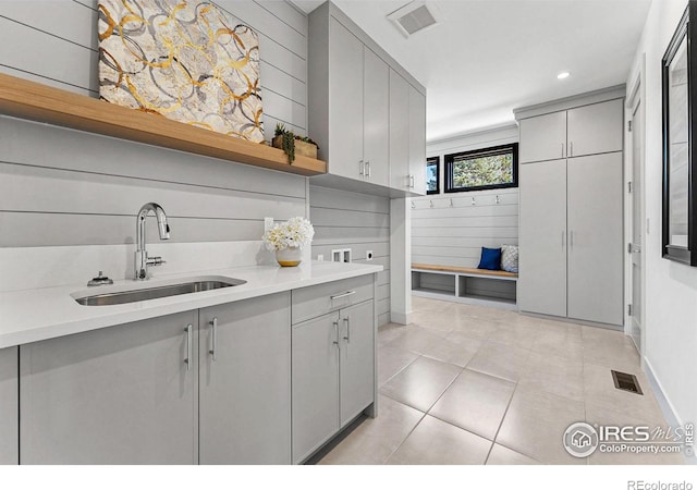 kitchen with wooden walls, gray cabinets, sink, and light tile patterned floors