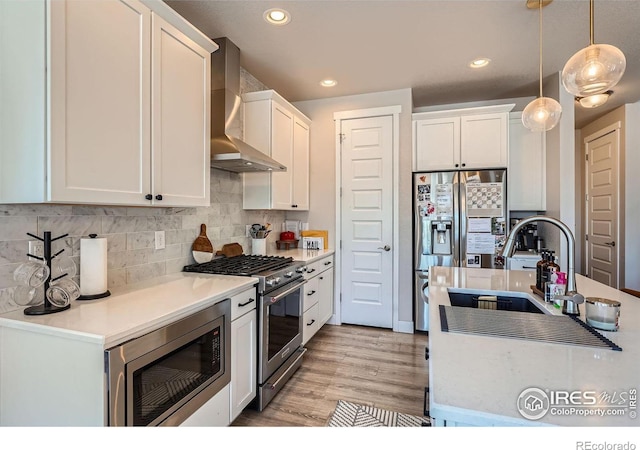 kitchen with wall chimney range hood, decorative light fixtures, stainless steel appliances, and white cabinets