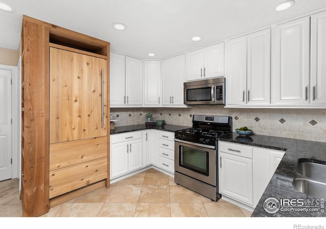 kitchen featuring light tile patterned flooring, appliances with stainless steel finishes, tasteful backsplash, white cabinetry, and dark stone counters