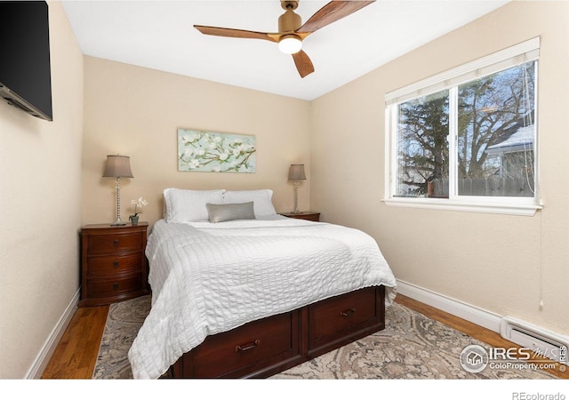 bedroom with ceiling fan, hardwood / wood-style floors, and a baseboard heating unit