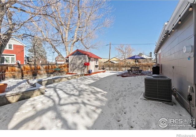 yard covered in snow with cooling unit, a storage shed, and a patio