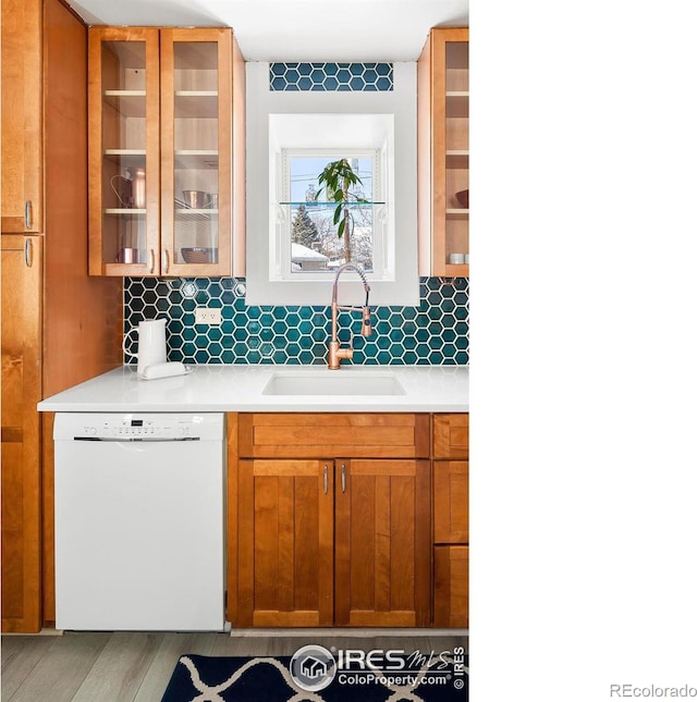 kitchen with light wood-type flooring, white dishwasher, sink, and backsplash