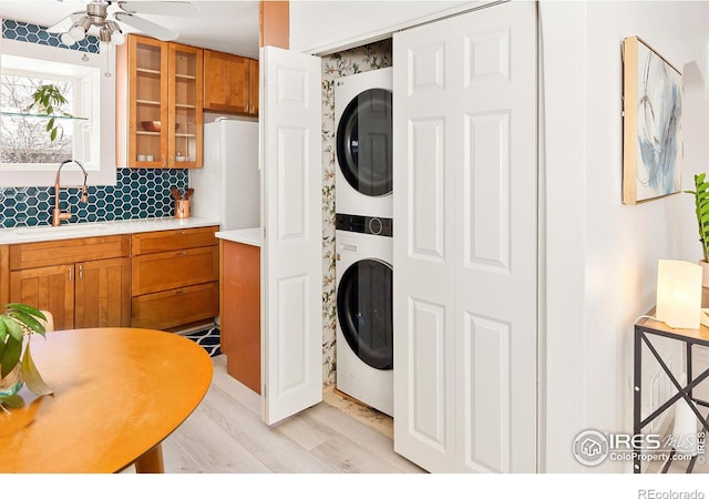 laundry area with ceiling fan, stacked washer and clothes dryer, sink, and light hardwood / wood-style flooring