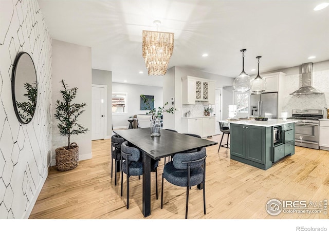 interior space with appliances with stainless steel finishes, decorative light fixtures, white cabinetry, a center island, and wall chimney exhaust hood