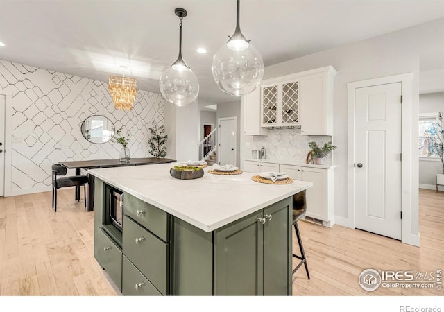 kitchen with light hardwood / wood-style flooring, a center island, green cabinetry, white cabinets, and decorative light fixtures