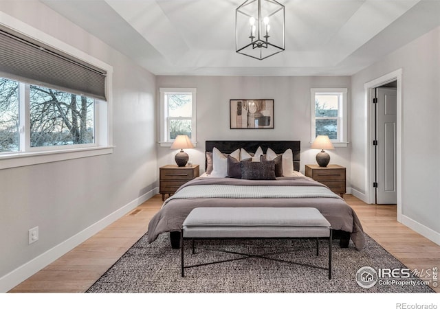 bedroom featuring light hardwood / wood-style flooring, an inviting chandelier, and a tray ceiling