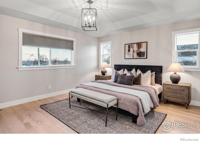 bedroom with a notable chandelier, a tray ceiling, and light wood-type flooring