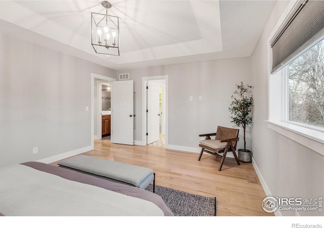 bedroom with connected bathroom, a notable chandelier, hardwood / wood-style floors, and a raised ceiling