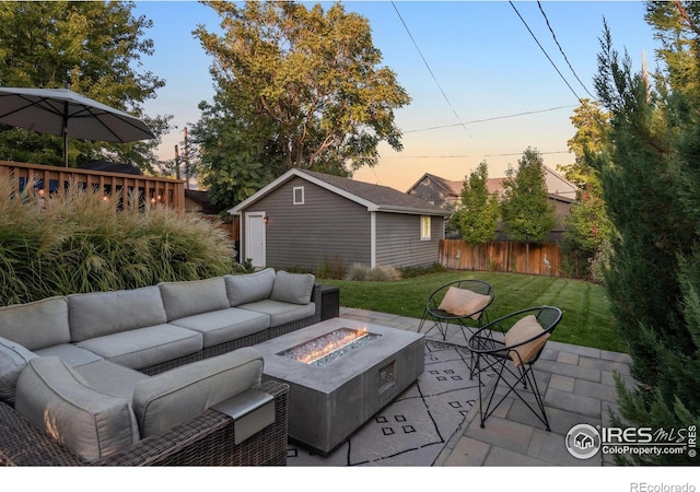 patio terrace at dusk with an outbuilding, a lawn, and an outdoor living space with a fire pit