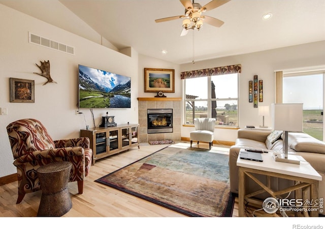 living room with ceiling fan, lofted ceiling, hardwood / wood-style floors, and a tile fireplace