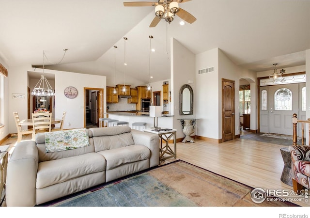 living room with ceiling fan with notable chandelier, high vaulted ceiling, and light hardwood / wood-style floors