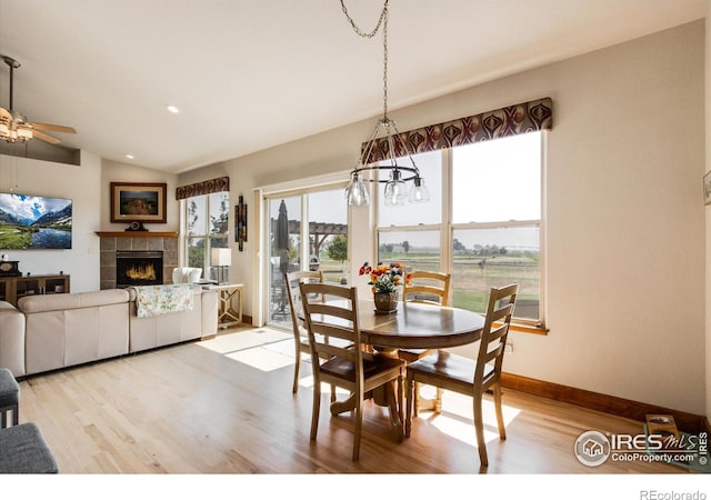 dining room featuring lofted ceiling, light hardwood / wood-style flooring, a tile fireplace, and ceiling fan