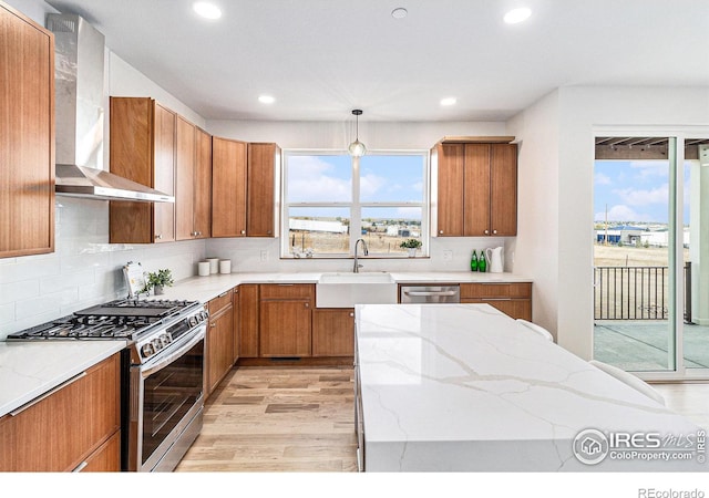 kitchen featuring stainless steel appliances, sink, backsplash, wall chimney range hood, and pendant lighting