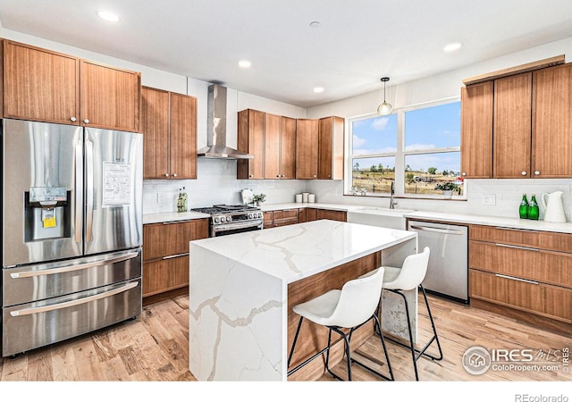 kitchen with a kitchen island, sink, appliances with stainless steel finishes, wall chimney range hood, and a breakfast bar area