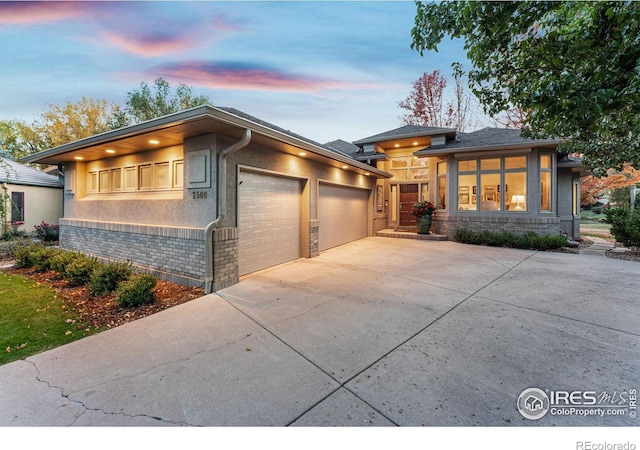 prairie-style house featuring a garage, driveway, brick siding, and stucco siding