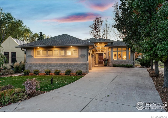 prairie-style house featuring brick siding, concrete driveway, roof with shingles, a front yard, and stucco siding