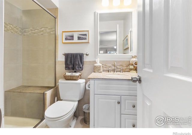 bathroom featuring tile walls, vanity, a shower with shower door, and toilet