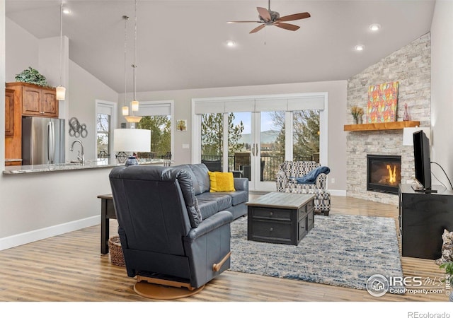 living room featuring a stone fireplace, sink, high vaulted ceiling, light wood-type flooring, and ceiling fan