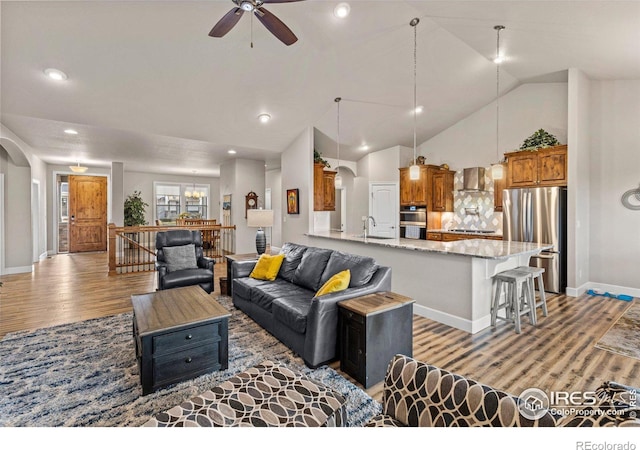 living room with high vaulted ceiling, sink, ceiling fan with notable chandelier, and light hardwood / wood-style floors