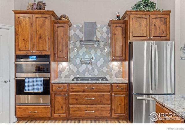 kitchen featuring light stone counters, wall chimney range hood, tasteful backsplash, and stainless steel appliances