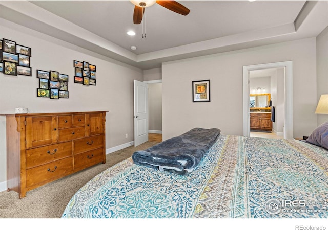 carpeted bedroom with a tray ceiling, ensuite bath, and ceiling fan