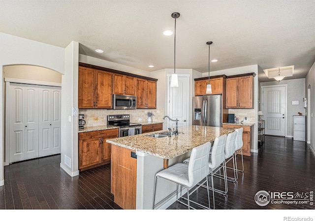 kitchen featuring pendant lighting, sink, a kitchen island with sink, stainless steel appliances, and light stone countertops