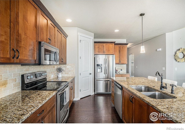 kitchen featuring appliances with stainless steel finishes, decorative light fixtures, sink, backsplash, and light stone countertops