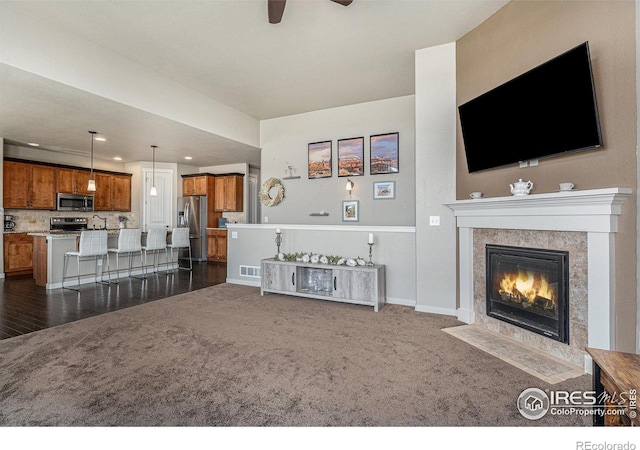 living room featuring a tile fireplace, ceiling fan, and dark colored carpet