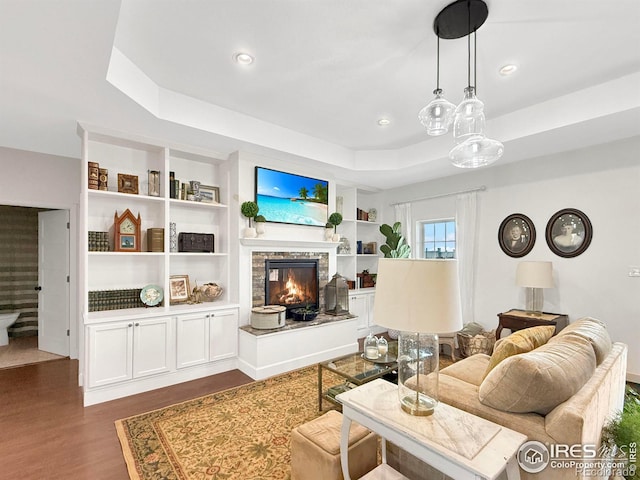 living room featuring a stone fireplace, dark hardwood / wood-style flooring, and a tray ceiling