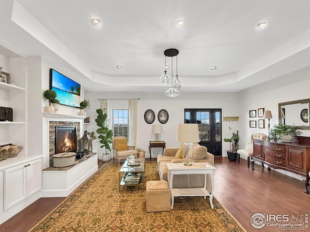 living room featuring dark wood-type flooring, a tray ceiling, and a stone fireplace