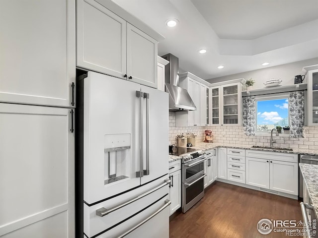 kitchen featuring high end white refrigerator, sink, white cabinetry, double oven range, and wall chimney range hood