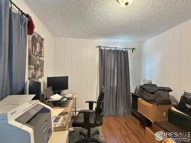 office area with wooden walls, light hardwood / wood-style floors, and a textured ceiling