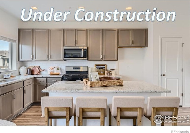 kitchen featuring a kitchen breakfast bar, stainless steel appliances, a center island, light stone counters, and decorative backsplash