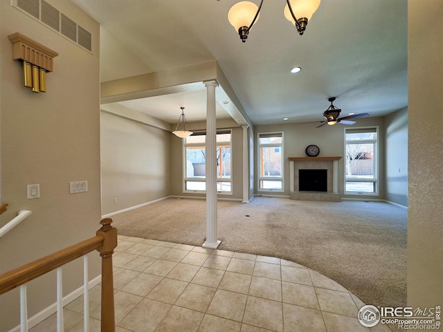 unfurnished living room with a tiled fireplace, ceiling fan, light carpet, and decorative columns